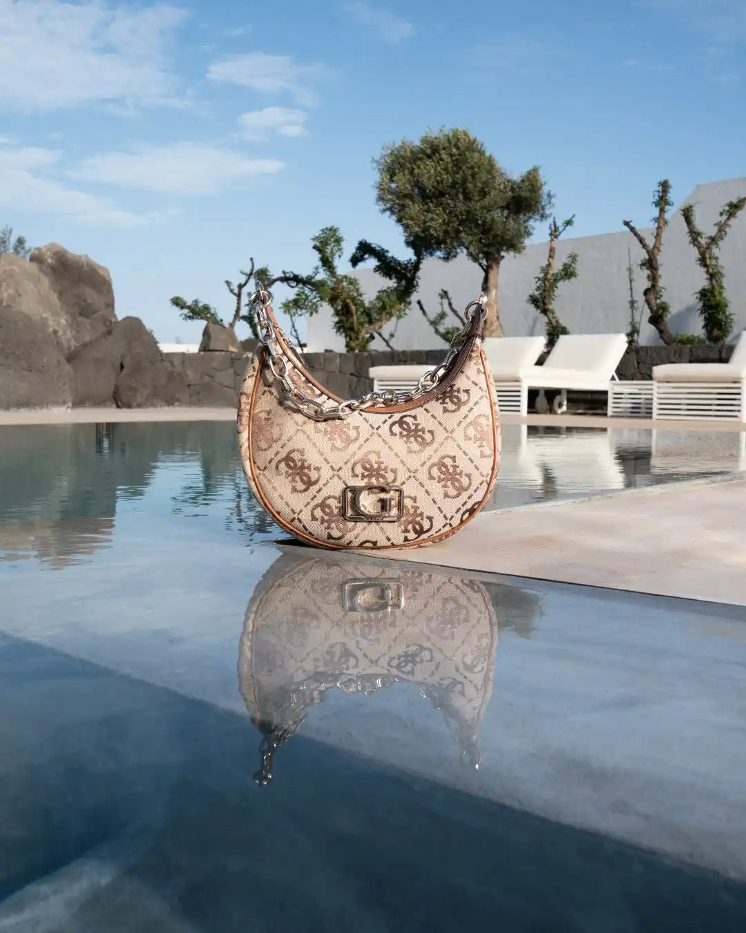Borsa Guess color beige e marrone a mezzaluna con un motivo di monogramma ripetuto.